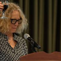 Woman behind podium raises glass of wine for a toast